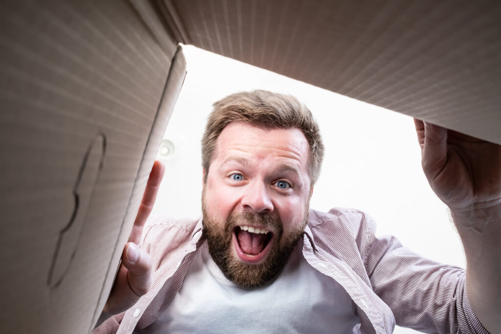 Happy man unpacked the delivered box with a parcel and shouts joyfully looking at the contents. Unpacking inside view. Happy man unpacked the delivered box with a parcel and shouts joyfully looking at the contents. Unpacking inside view.